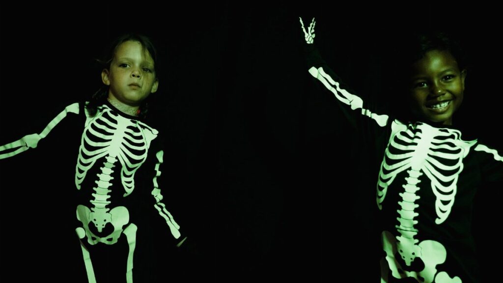 Two children wearing skeleton costumes for Halloween, smiling in a studio.
