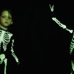 Two children wearing skeleton costumes for Halloween, smiling in a studio.
