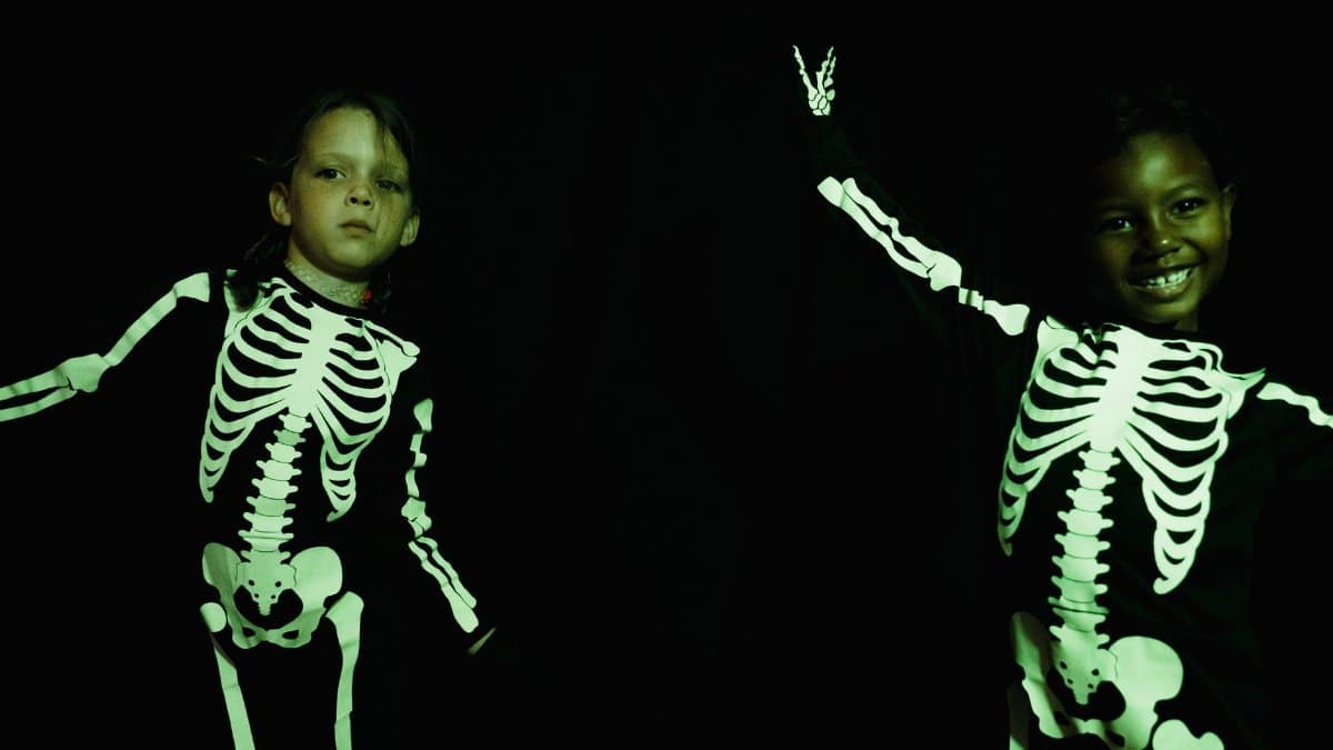 Two children wearing skeleton costumes for Halloween, smiling in a studio.