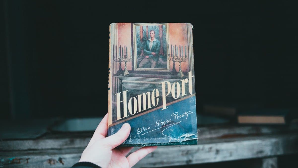Crop unrecognizable person demonstrating retro textbook with painting and title on paper cover in daytime