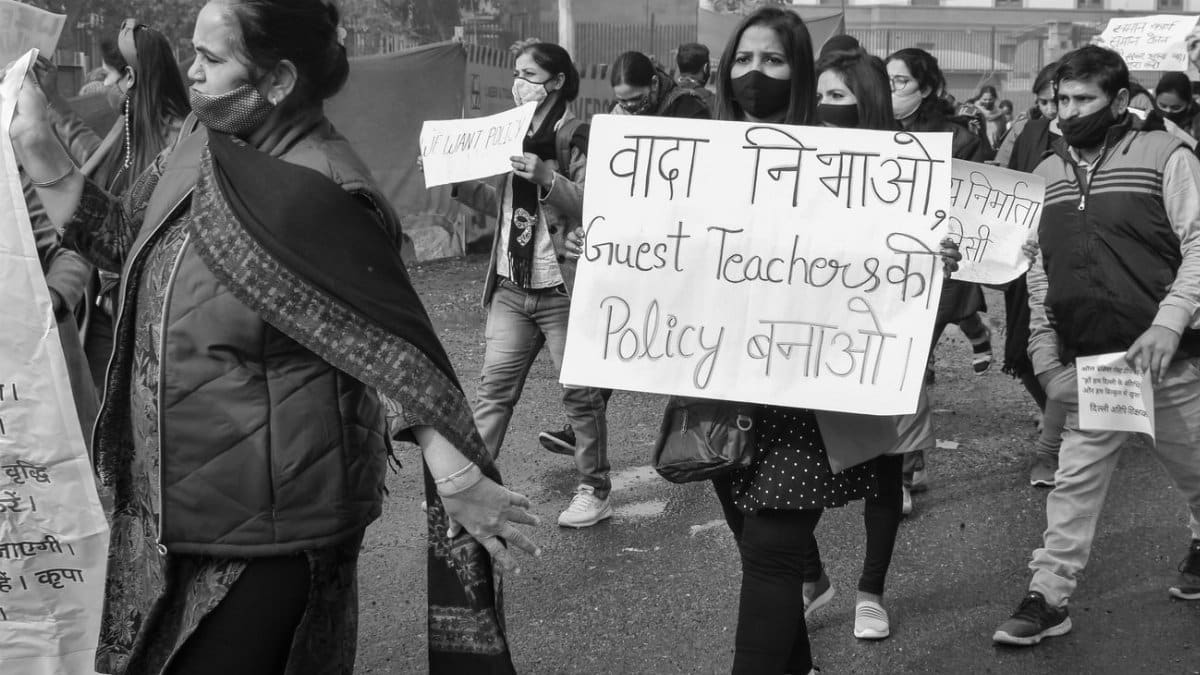 Black and white photo of a street protest for guest teacher policy reform, featuring diverse participants.