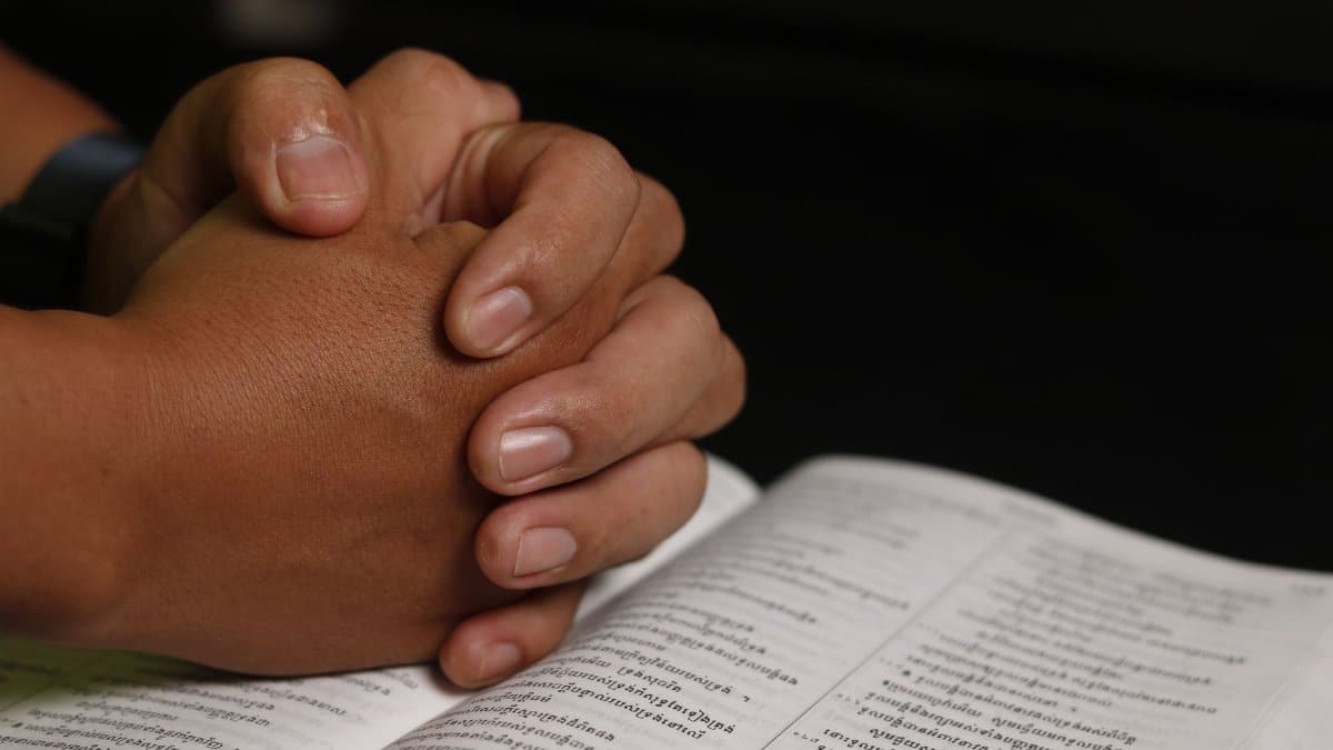 Close-up of hands in prayer over an open Khmer Bible, symbolizing faith and worship.