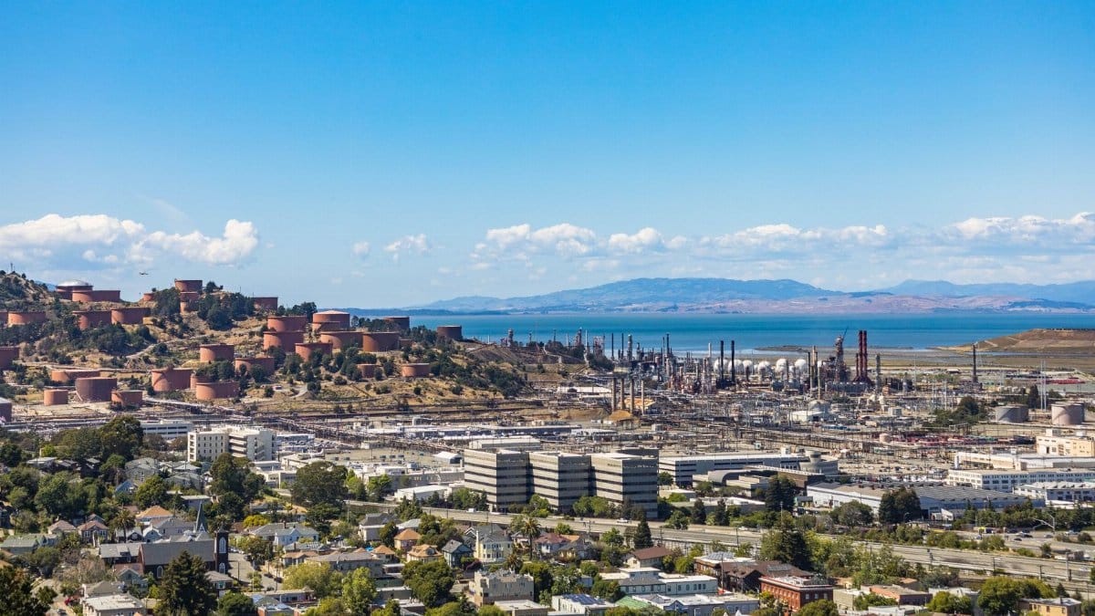 Aerial view of an urban area with an oil refinery by the sea and mountains.