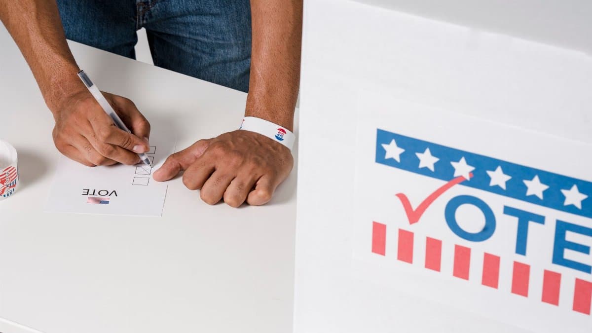 A person casting a vote with a ballot near a marked voting box, emphasizing civic participation.