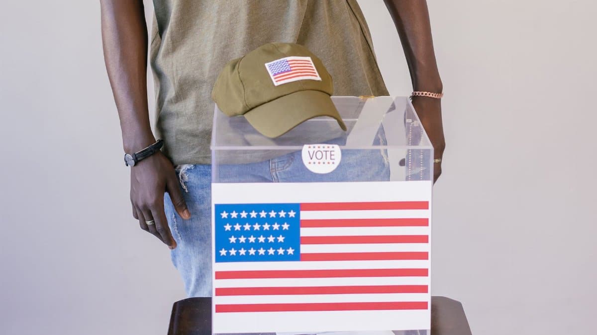 Adult voter standing by a ballot box with American flag, symbolizing democracy and election participation.