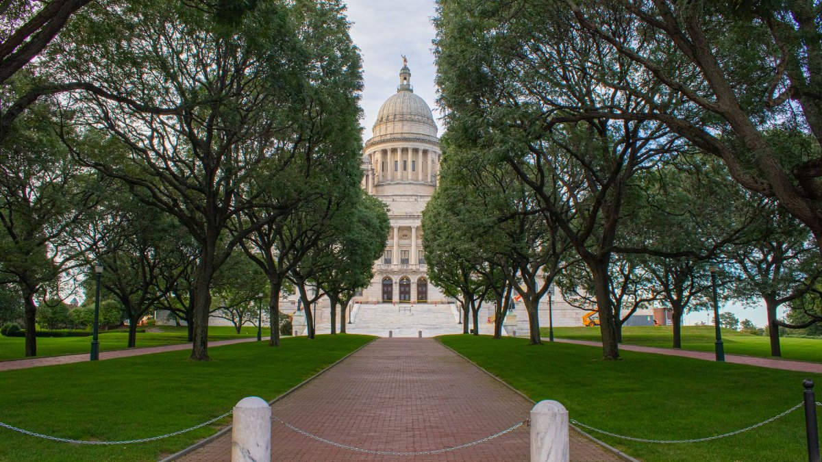 The majestic Rhode Island State House surrounded by lush green trees on a sunny summer day.
