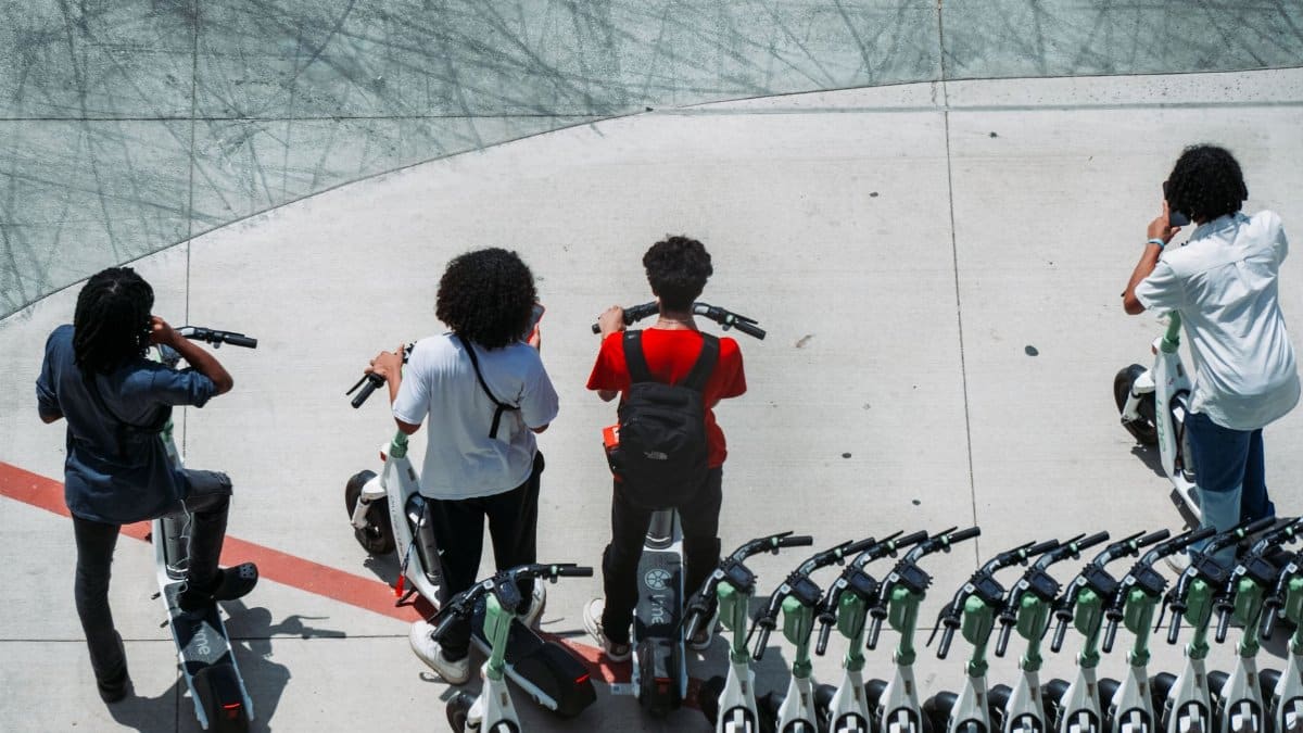 Group of young adults using electric scooters on a sunlit urban pavement.