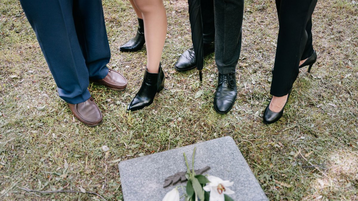 Shoes of mourners gathered around a gravestone with lilies in a cemetery.