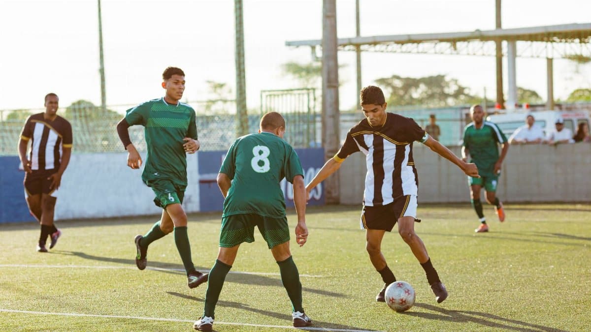 Five male soccer players in action during a daytime soccer match on an outdoor field.