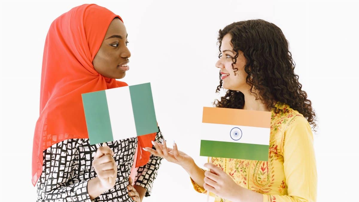 Two women with Nigerian and Indian flags engaging in friendly cultural exchange.