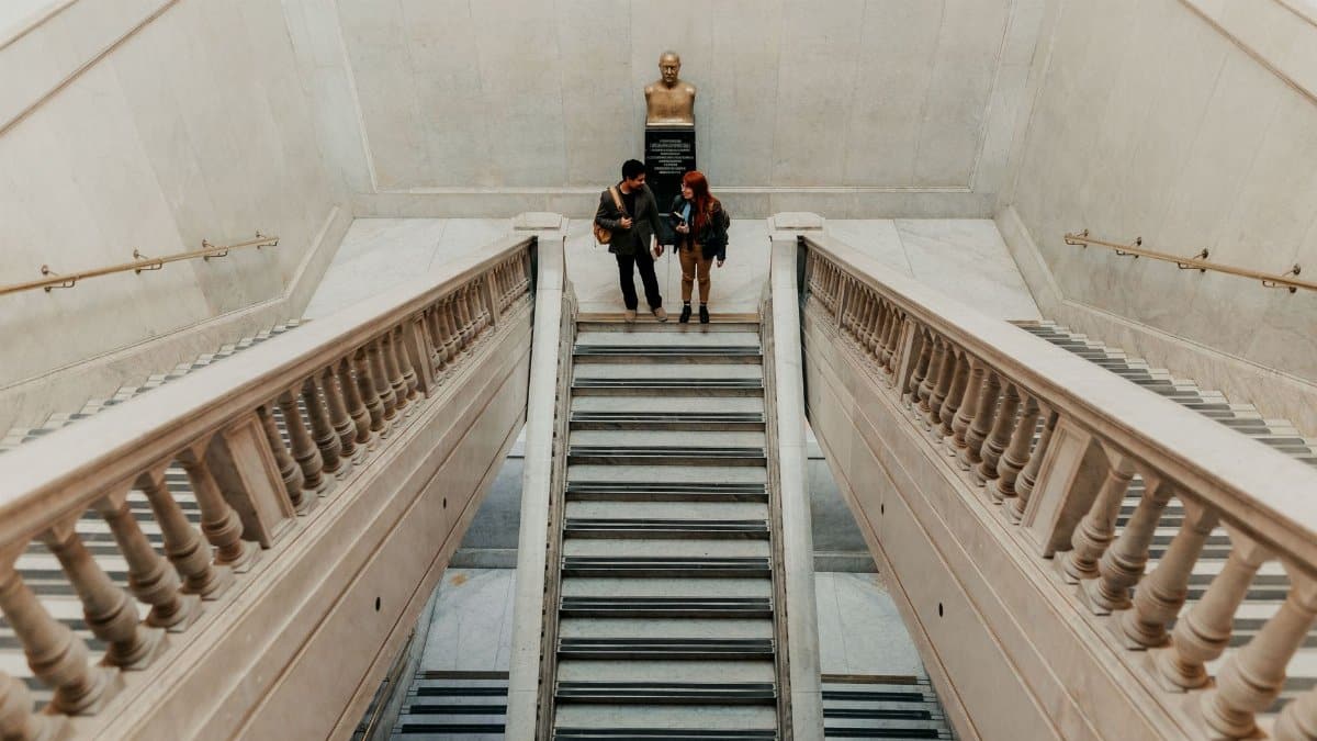 Two students walk down a grand marble staircase in a historic building in Buenos Aires.