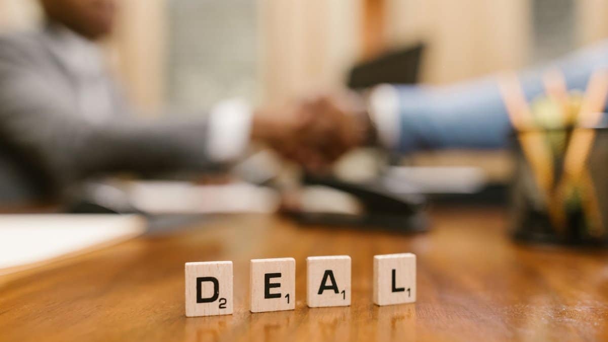 Close-up of Scrabble tiles spelling 'deal' with a handshake in the background.