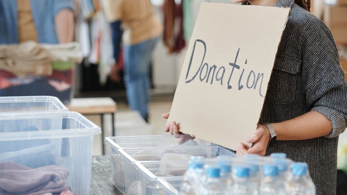 A volunteer holds a cardboard donation sign at a charity event with donation boxes ready for collection.