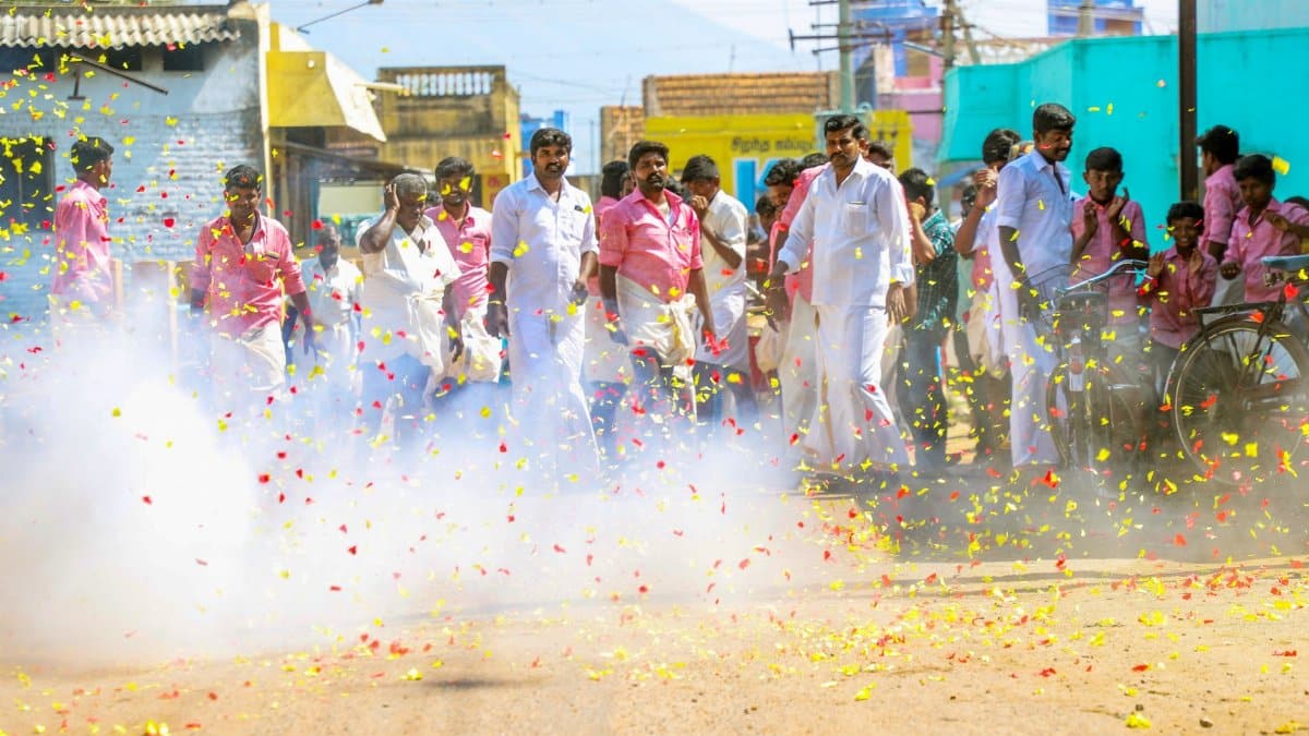 Vibrant street celebration with people amidst firecrackers and colorful confetti during the day.