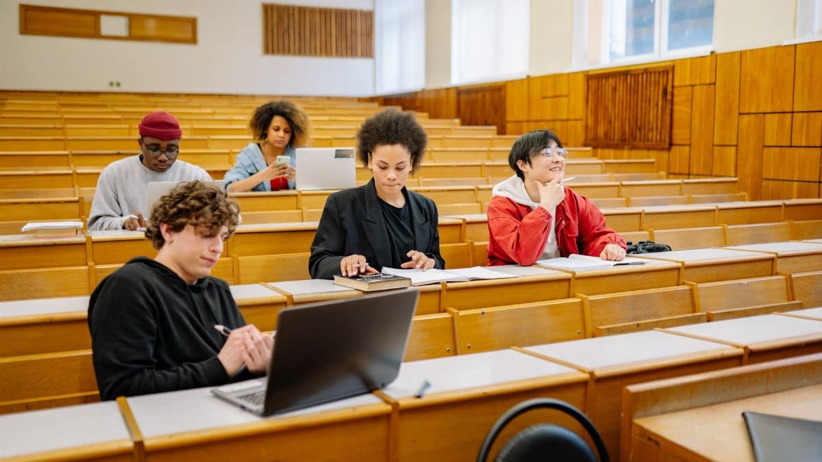 Group of college students studying together in a classroom, focused on learning with laptops and books.