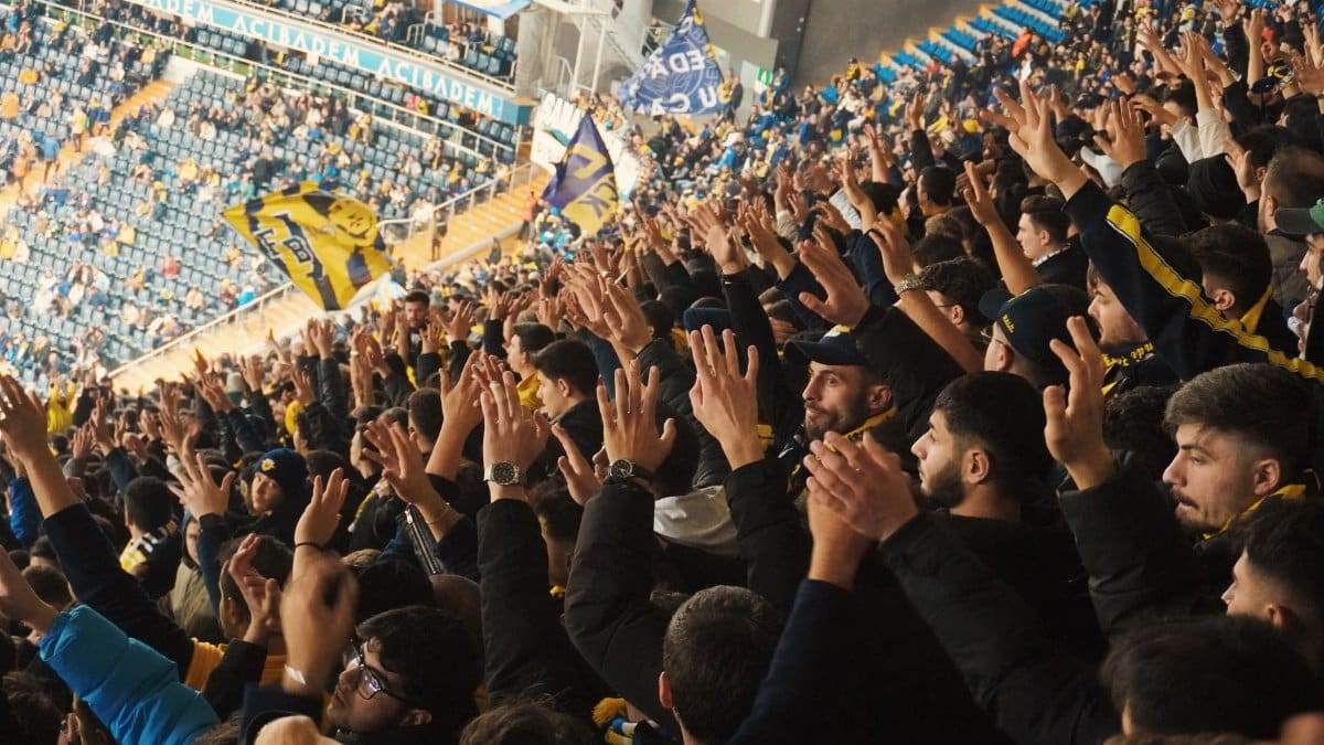 Energetic fans with raised hands in a stadium, supporting their soccer team with enthusiasm.