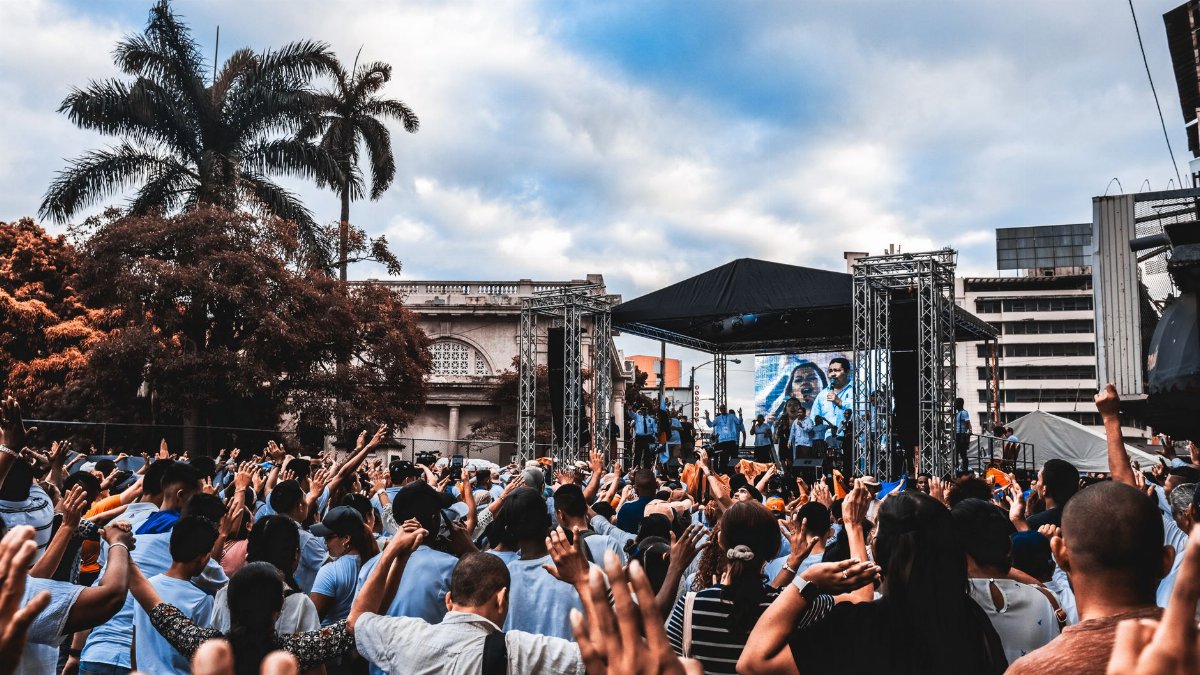 Dynamic scene at an outdoor concert with a large, enthusiastic crowd raising their hands.