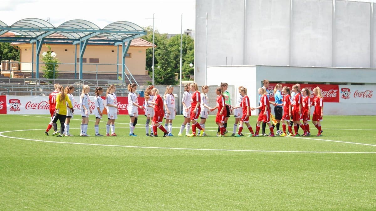 Young women's soccer teams in uniforms shaking hands on the field, promoting sportsmanship.