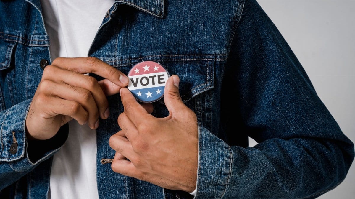 A person pinning a 'VOTE' button on a denim jacket symbolizing civic engagement.