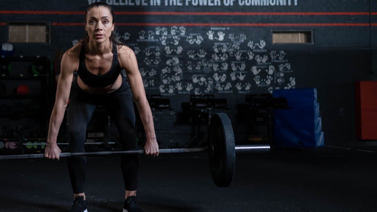 Fit woman performing deadlift in a gym with emphasis on strength and community.