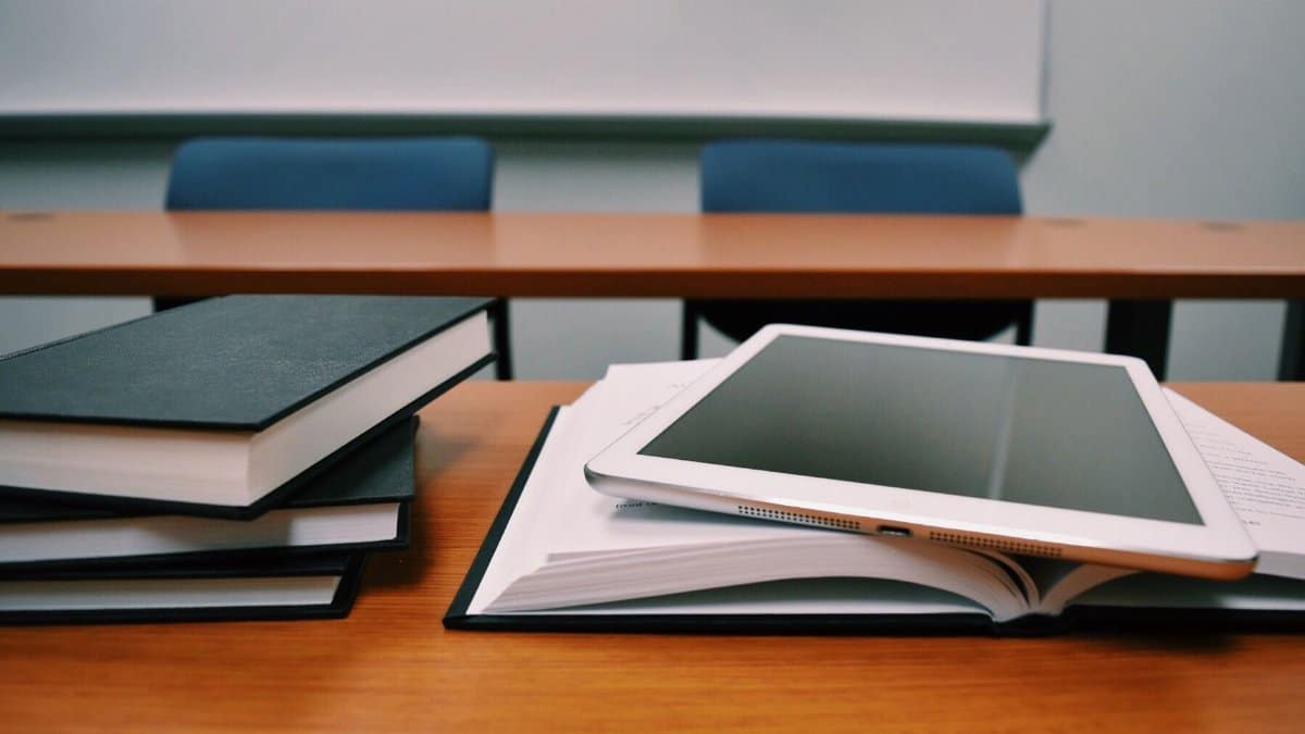 Books and a tablet on a desk in a classroom, depicting modern education.