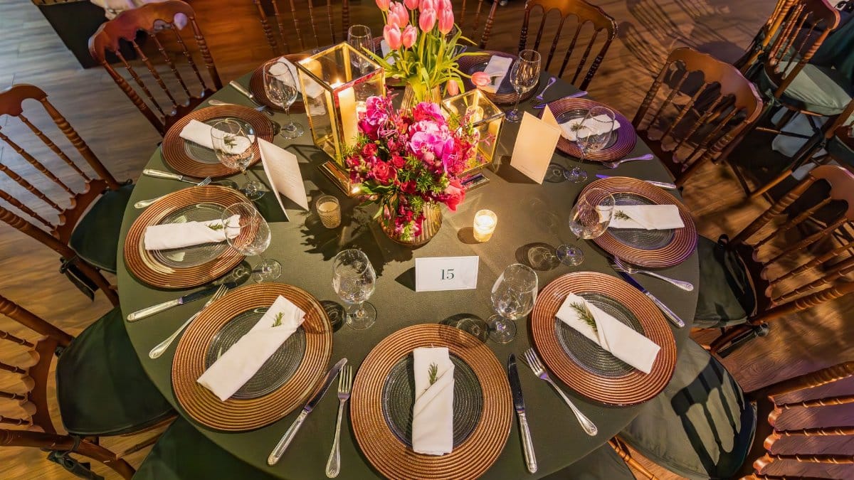 An elegantly decorated round table for a wedding or event, featuring flowers, candles, and fine dining settings.