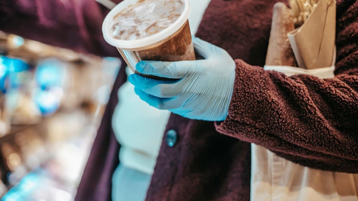 Crop anonymous female buyer in gloves with plastic container of frozen food in grocery store during coronavirus pandemic