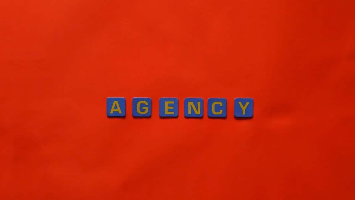Blue letter tiles spelling 'AGENCY' on a vibrant red background, ideal for creative promotion.