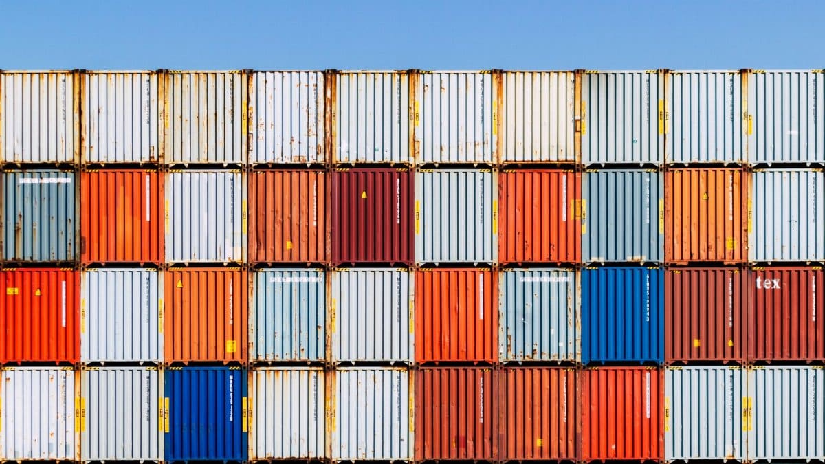 Colorful stacked shipping containers against a vibrant blue sky, conveying global trade and logistics.