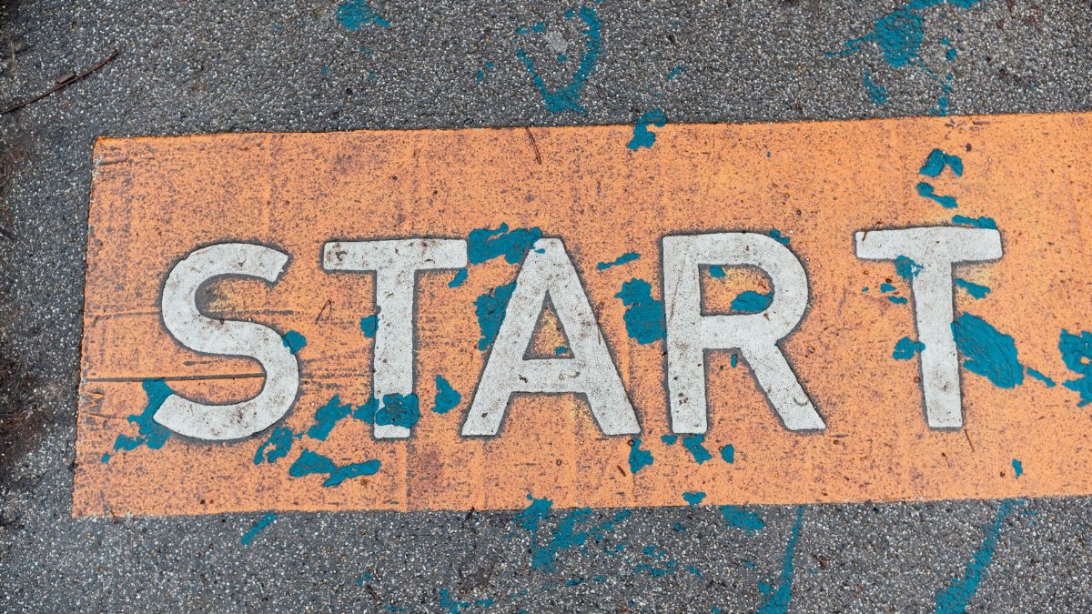 A worn orange start line painted on urban pavement with blue splatters.