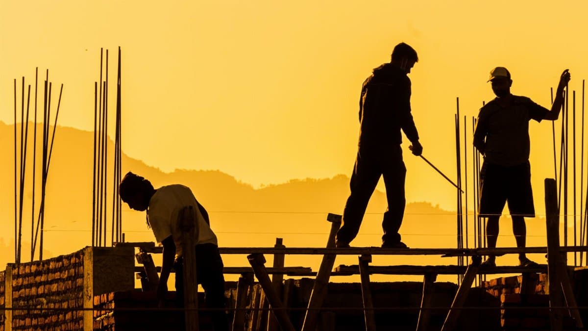Silhouetted workers on a construction site at sunset, highlighting the manual labor involved.