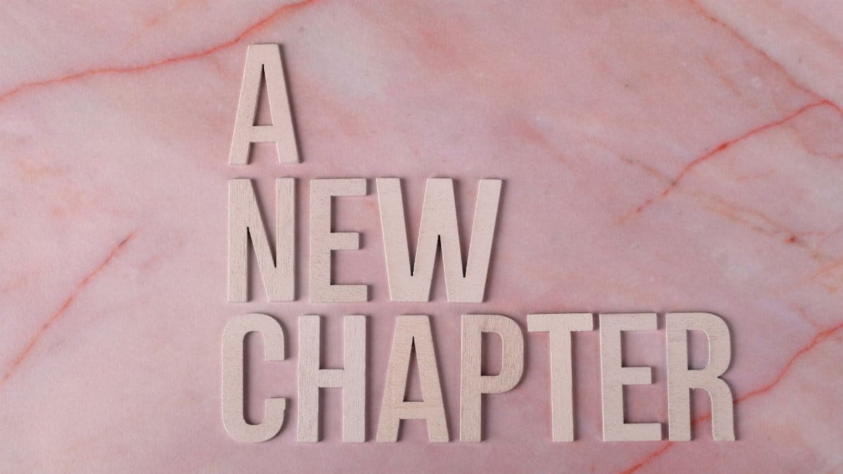 Wooden letters spell 'A New Chapter' on a pink marble background, symbolizing beginning.