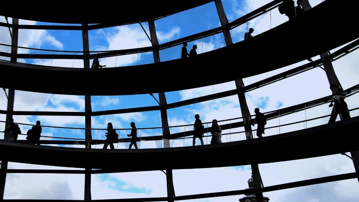 Silhouettes of people walking inside Reichstag's glass dome in Berlin, Germany, showcasing architectural beauty.