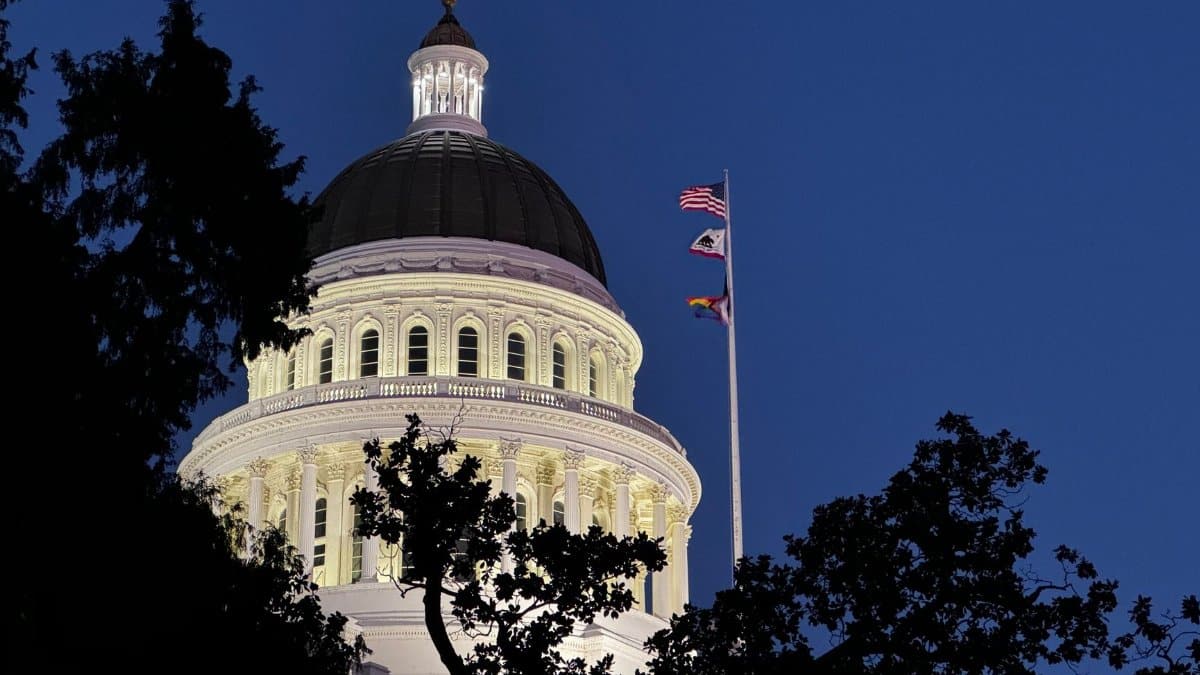 Illuminated California State Capitol dome against a clear night sky with fluttering flags.