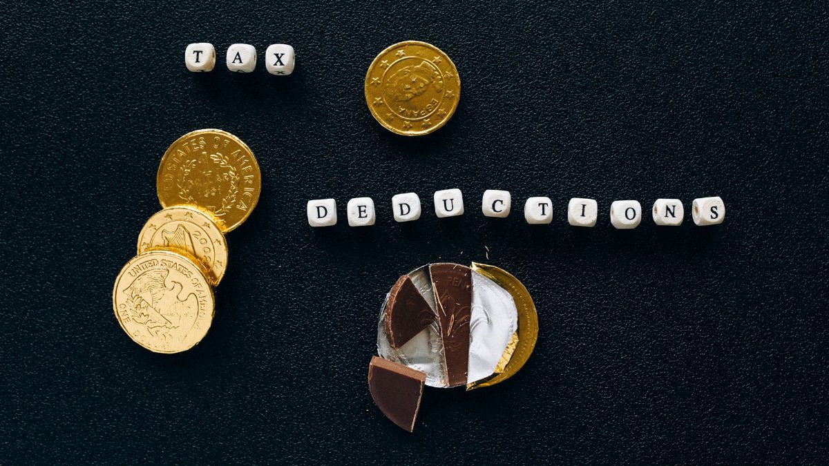 Creative concept of tax deductions using chocolate coins and letter tiles on a black background.