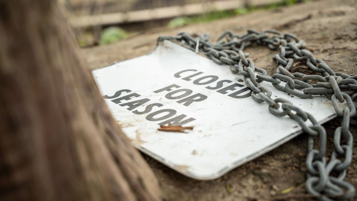 A chained sign reading 'Closed for Season' in a natural park environment, indicating restricted access.