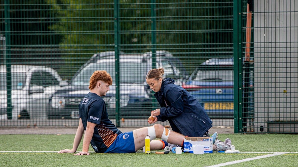 A sports therapist tends to an injured athlete on an outdoor football field.