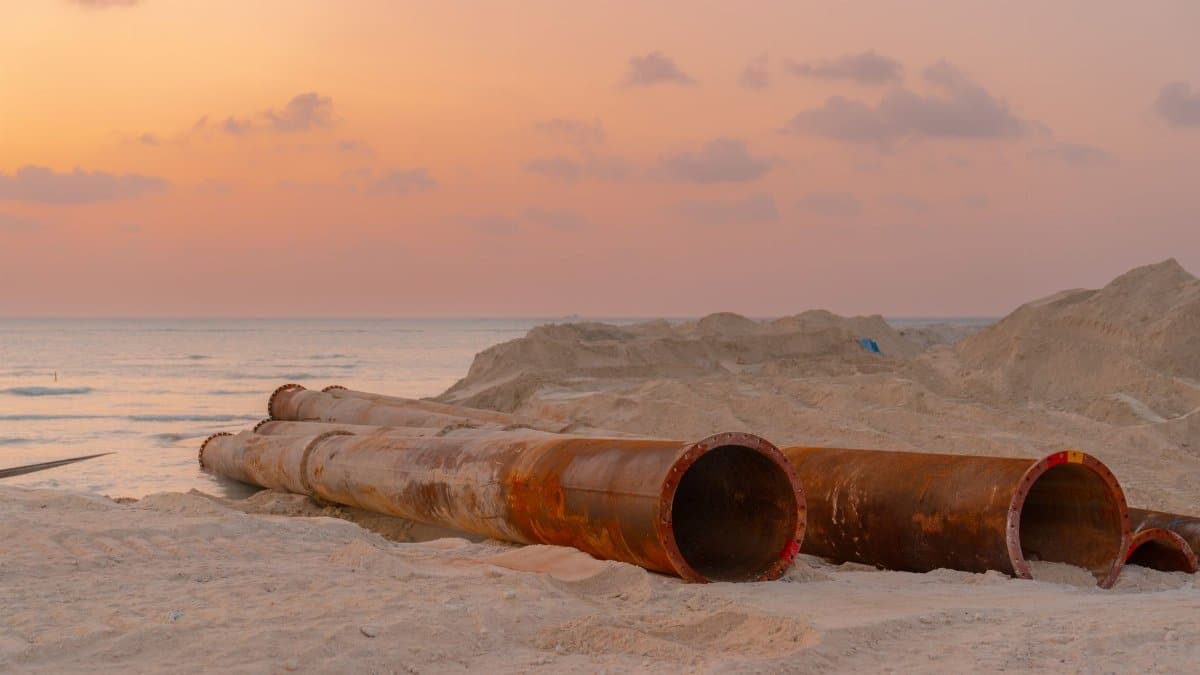 Rusty pipes at a coastal construction site with scenic sunset view.