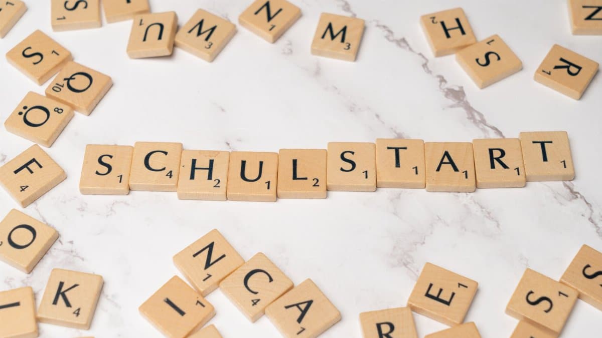 Wooden tiles forming the word 'Schulstart' on a marble surface, symbolizing school beginning.