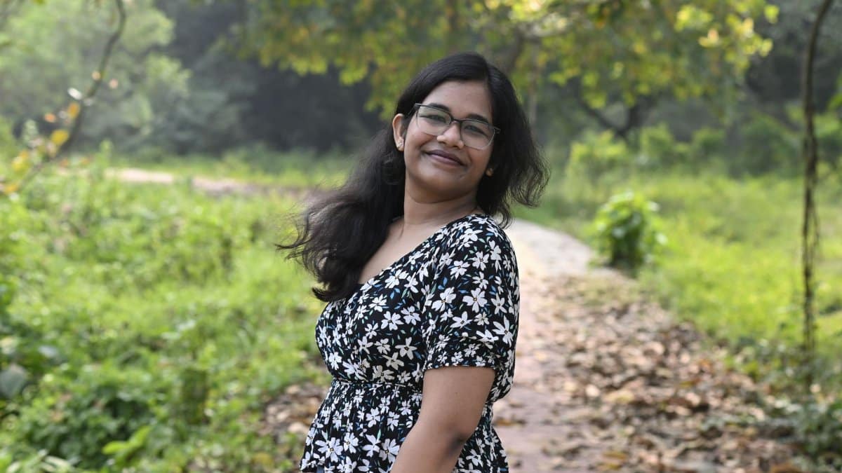 A woman smiling outdoors on a leafy path amid lush greenery.