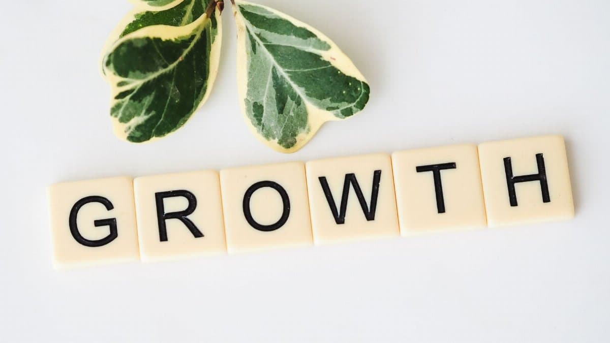 Close-up image of Scrabble tiles spelling 'Growth' with green leaves on a white background.
