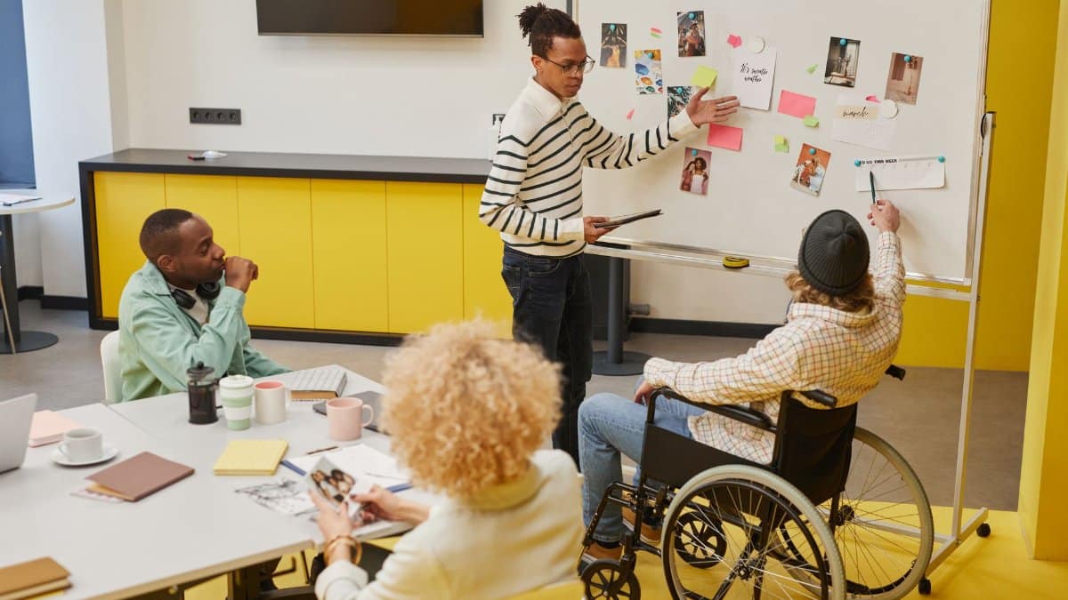 A diverse group of professionals in a creative workspace discussing ideas and planning on a whiteboard.