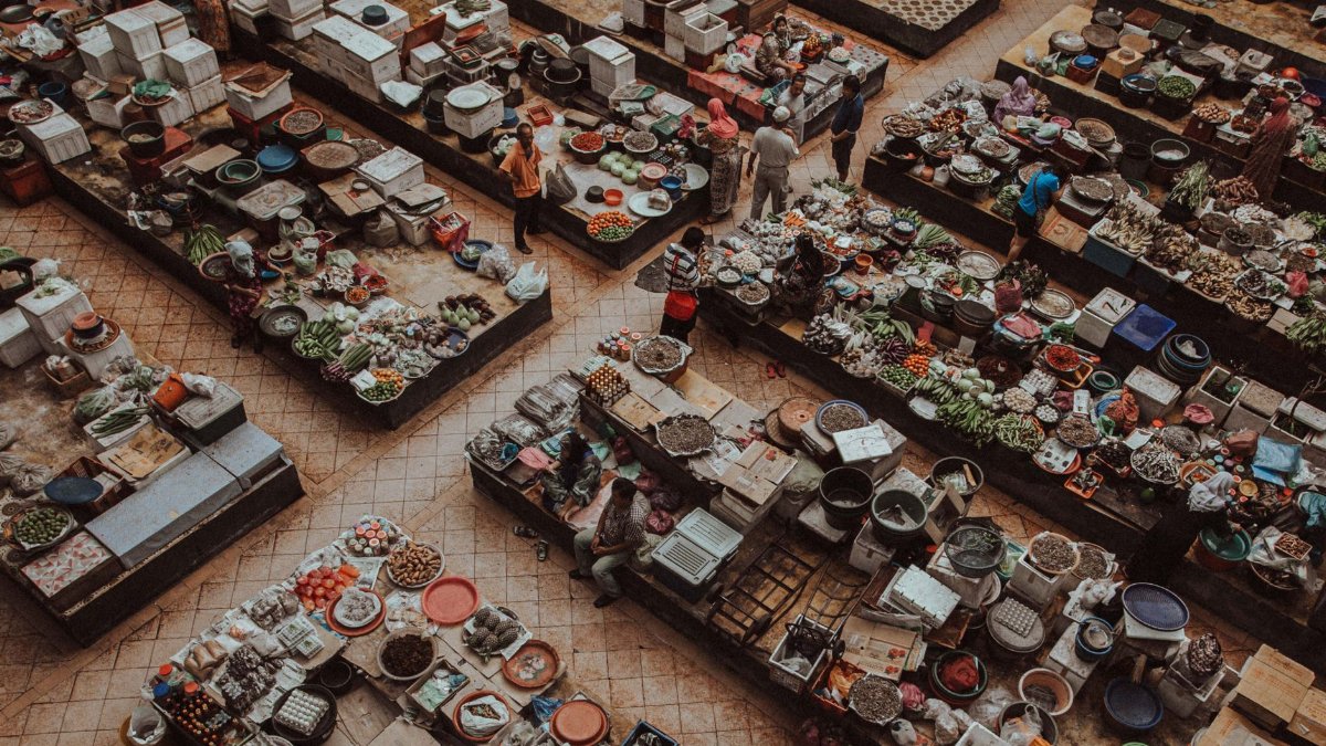 A bustling overhead view of an urban market with various stalls selling fresh produce and goods.