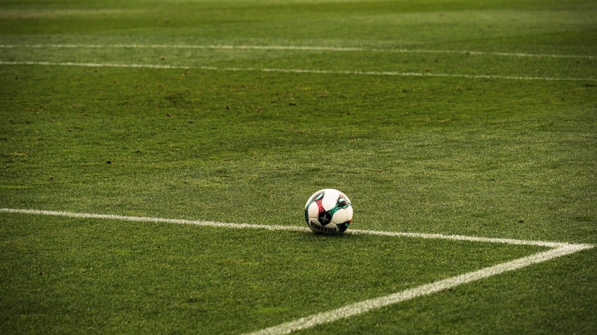 A soccer ball rests on a well-maintained green football field corner, ready for play.