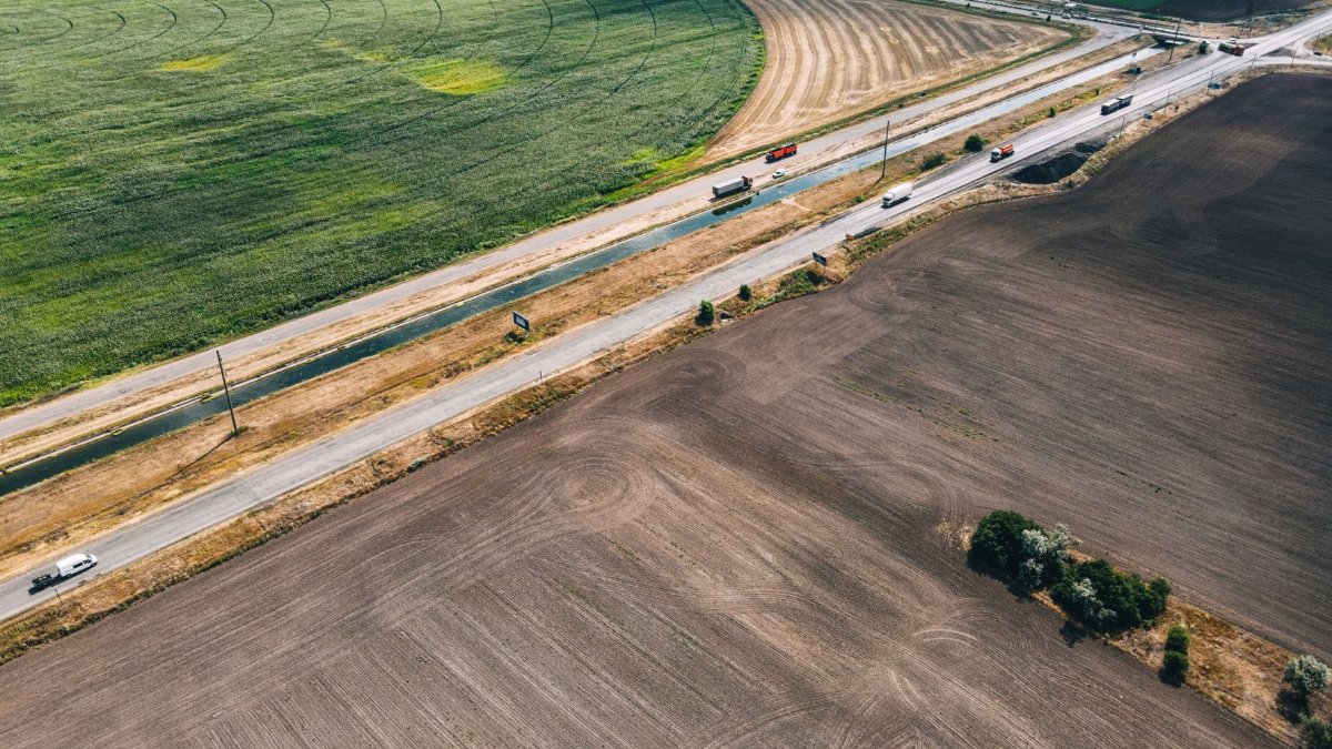 A high-angle aerial photo capturing vibrant agricultural fields intersected by a busy road with vehicles.