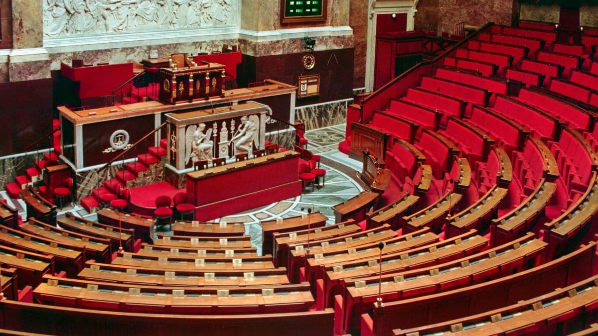 Bright and elegant view of the French National Assembly's rich interior with red seats and ornate decor.