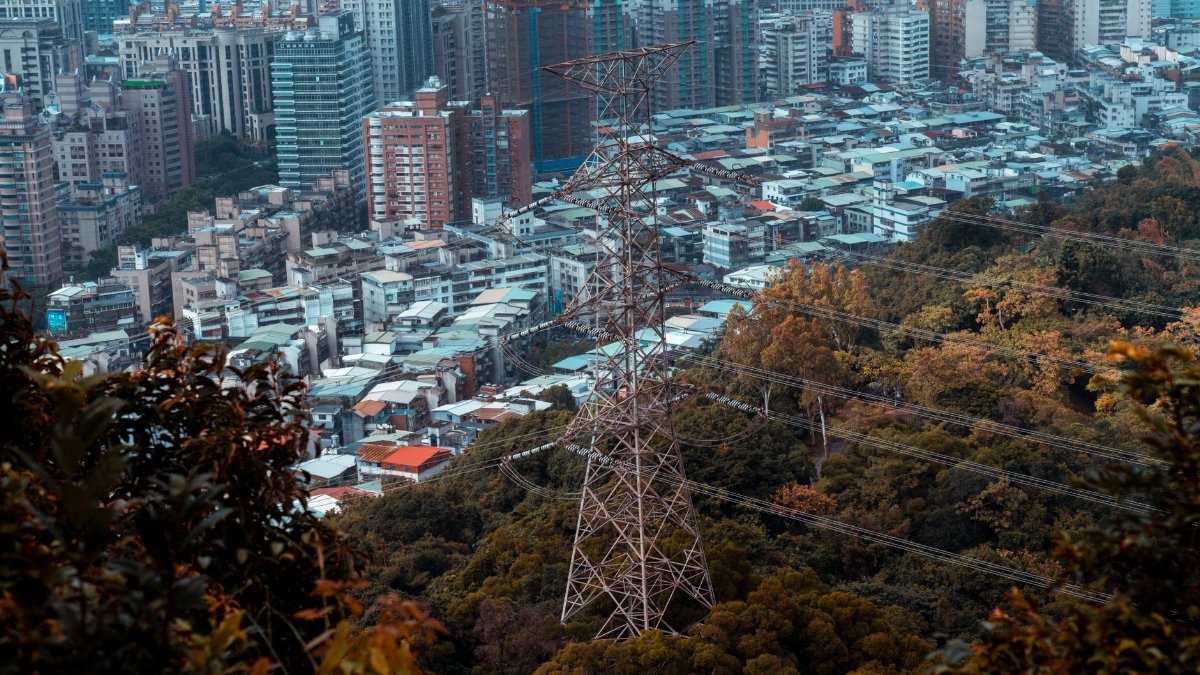 Aerial view of city buildings adjacent to forest with power lines in foreground.