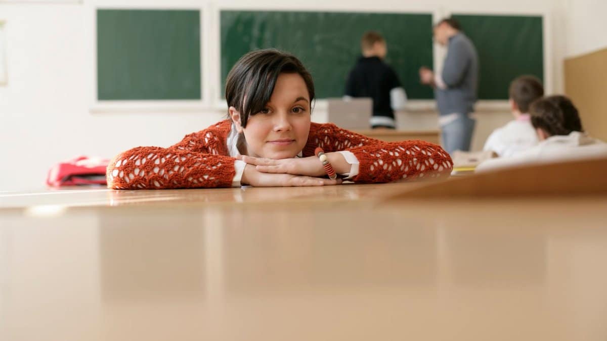A young student rests her head on a desk in a classroom, with a focus on education and relaxation.