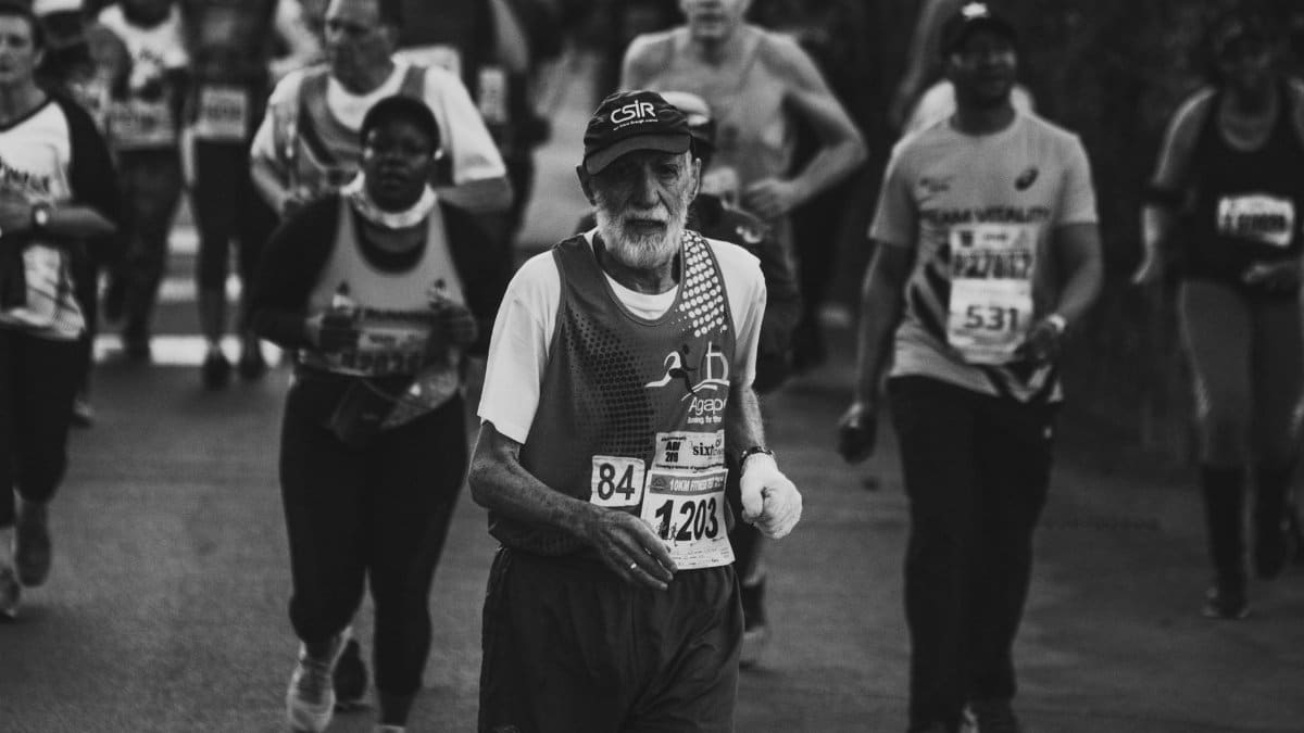 A senior man running in a marathon surrounded by other participants, depicted in a black and white image.