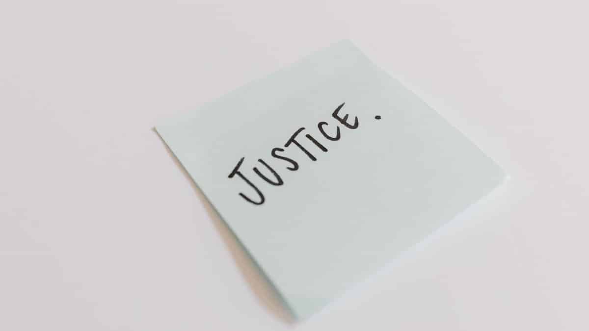 A close-up shot of a sticky note with the word 'Justice' handwritten on it.